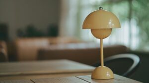 A single small yellow portable lamp sitting alone on a wooden table, softly lit, with nothing else around it