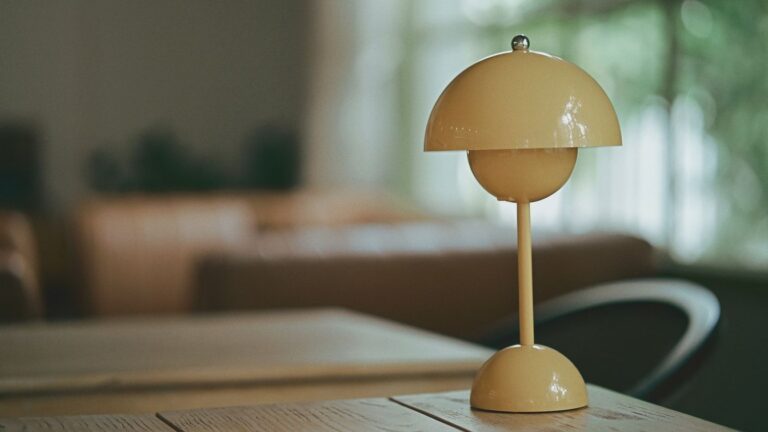 A single small yellow portable lamp sitting alone on a wooden table, softly lit, with nothing else around it