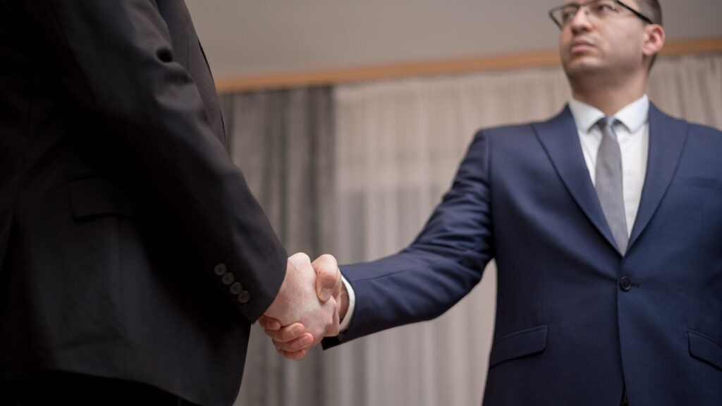 Two business professionals in suits shaking hands, formal indoor setting