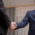 Two business professionals in suits shaking hands, formal indoor setting