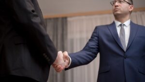 Two business professionals in suits shaking hands, formal indoor setting