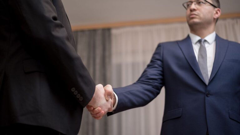 Two business professionals in suits shaking hands, formal indoor setting