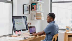 A developer focused on dual screens at a bright home office desk, reviewing information before making a decision