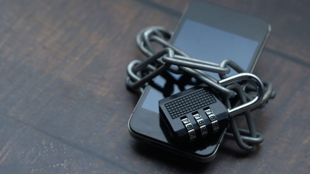 A smartphone wrapped in a chain and secured with a combination padlock, symbolizing locked-down digital security