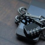 A smartphone wrapped in a chain and secured with a combination padlock, symbolizing locked-down digital security