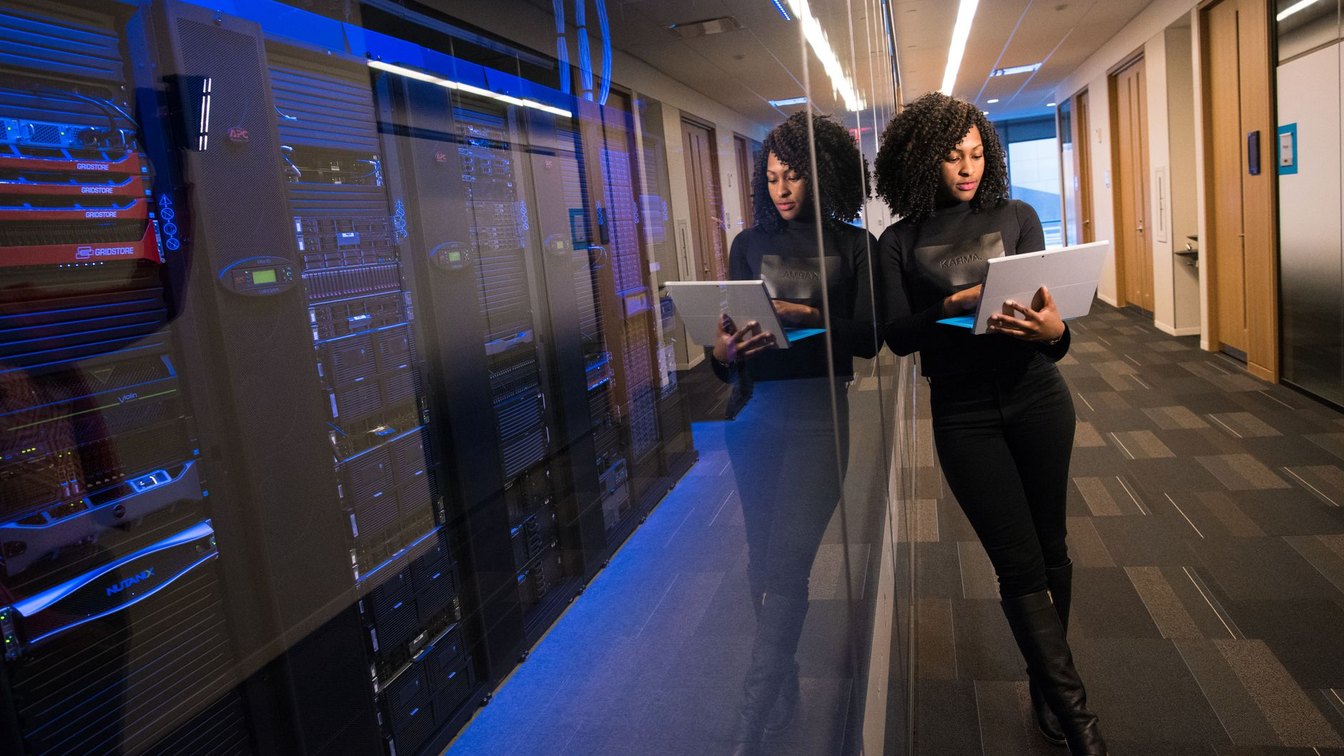 An engineer checking a laptop in a data center corridor lined with server racks