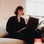 Woman working on a laptop on a sofa in a bright, warm living room