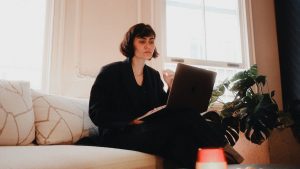 Woman working on a laptop on a sofa in a bright, warm living room
