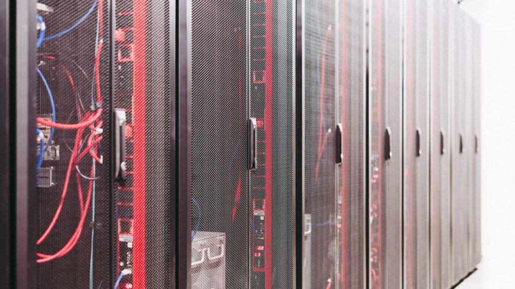 A dim data center aisle at night with rows of server racks, one rack unit glowing an alarm-red color among the others