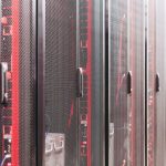 A dim data center aisle at night with rows of server racks, one rack unit glowing an alarm-red color among the others