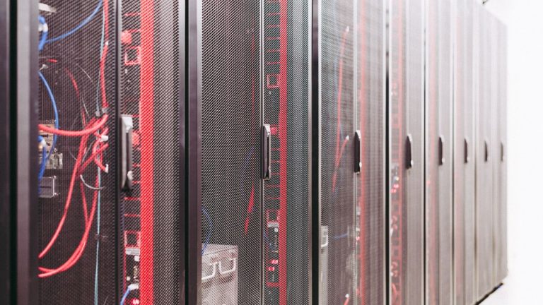 A dim data center aisle at night with rows of server racks, one rack unit glowing an alarm-red color among the others