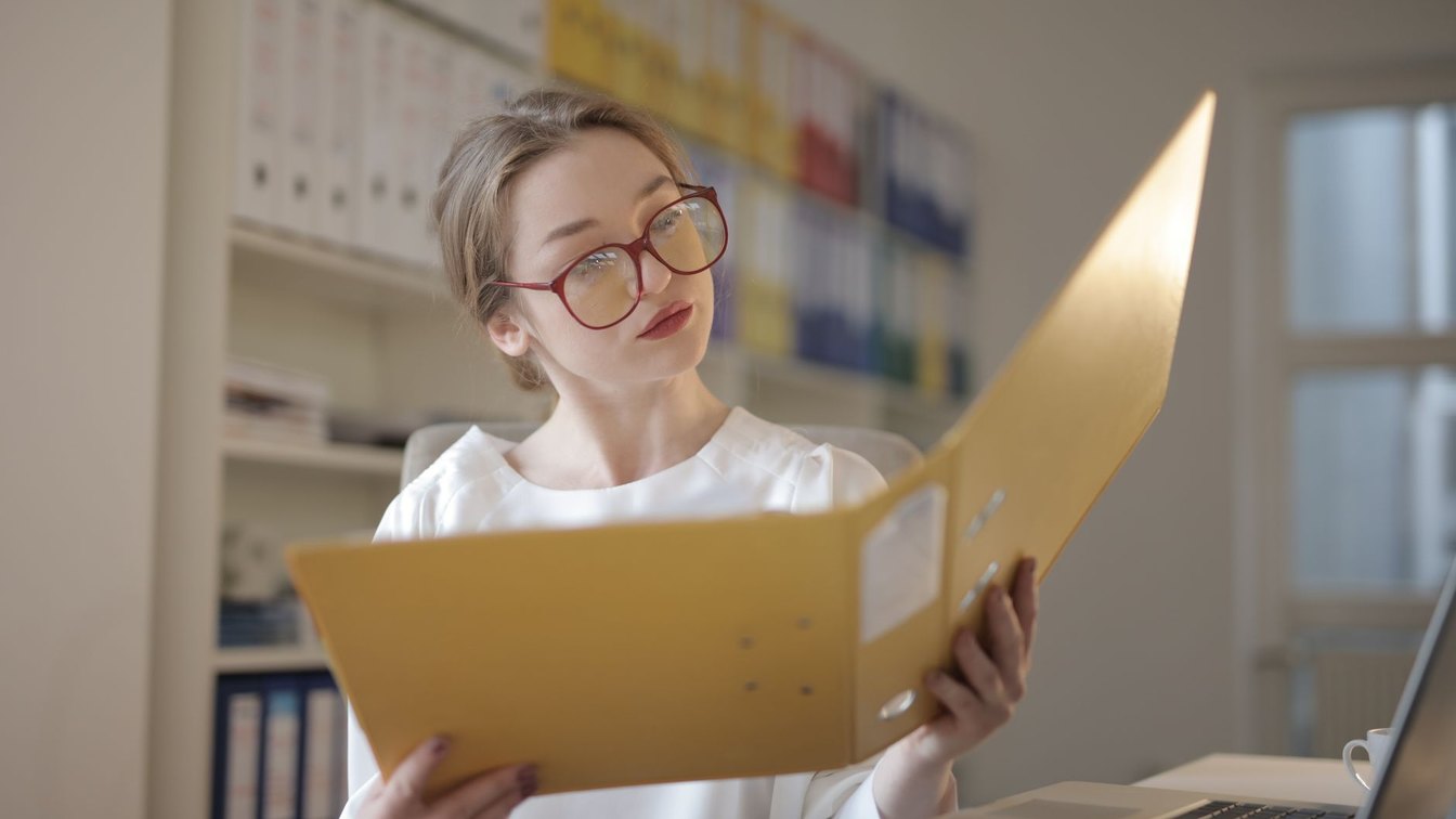 Woman reading through a folder of documents at an office desk