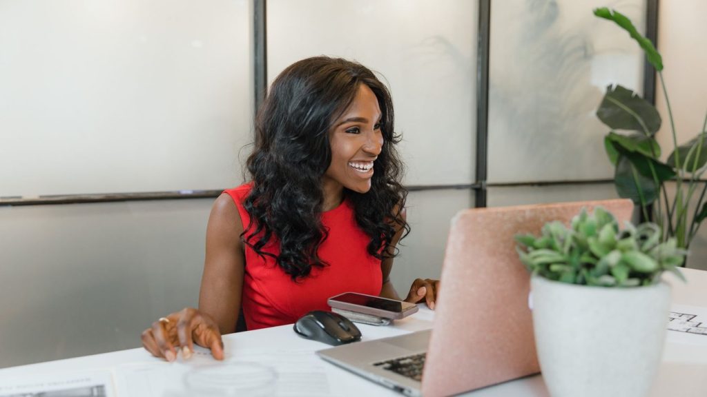 Smiling professional working on a laptop at a bright desk with a plant nearby