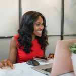 Smiling professional working on a laptop at a bright desk with a plant nearby