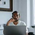 A person sitting at a laptop in a bright, minimalist home office, thinking