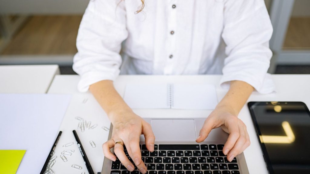 Close-up of a person's hands typing on a laptop keyboard in a bright, modern office