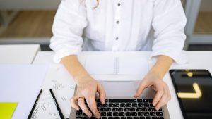 Close-up of a person's hands typing on a laptop keyboard in a bright, modern office