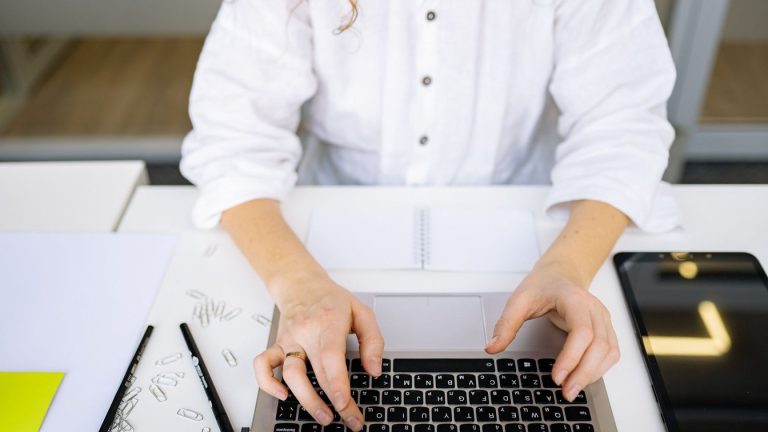Close-up of a person's hands typing on a laptop keyboard in a bright, modern office